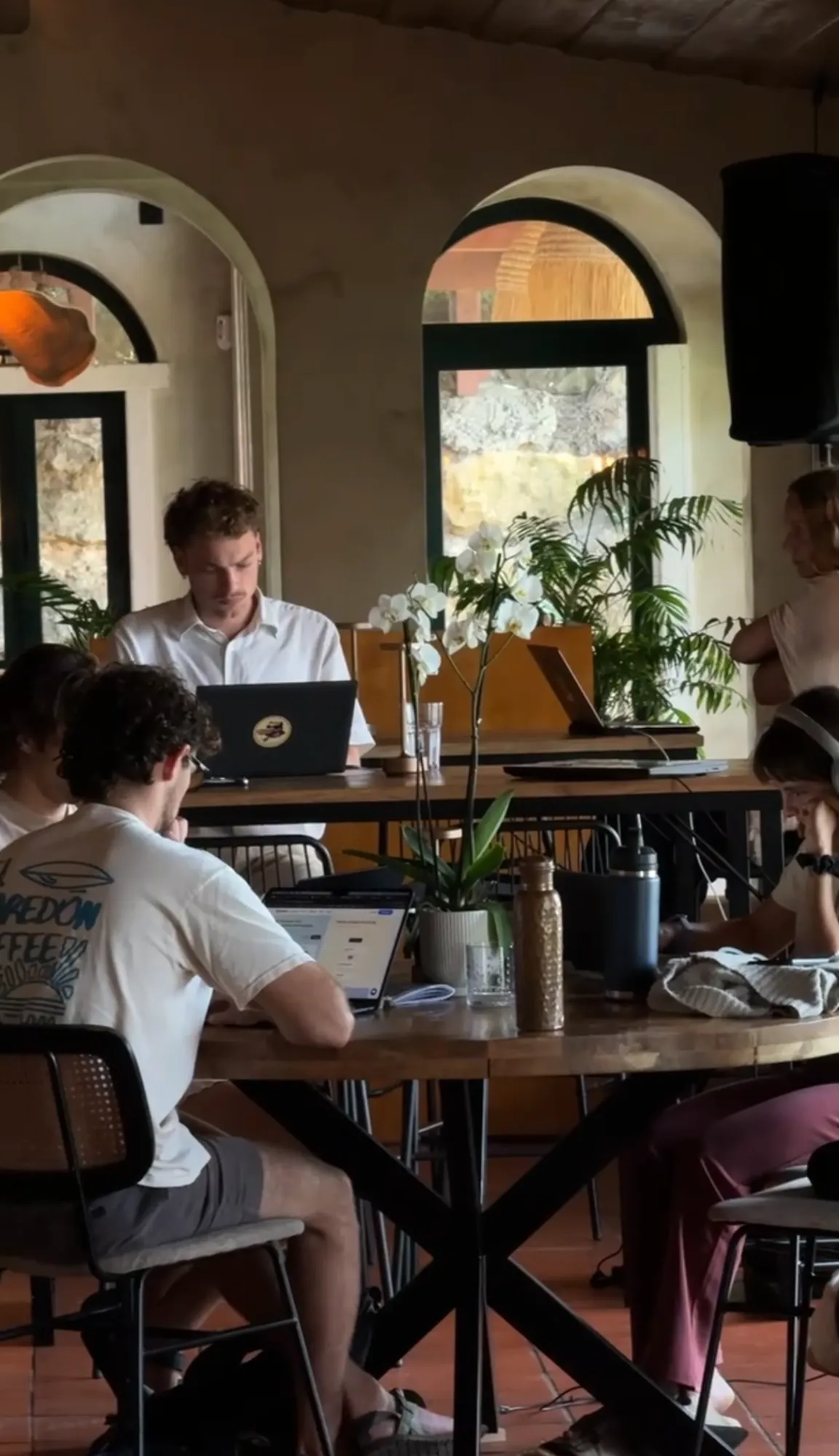 A team heads-down on laptops at a long table by arched windows